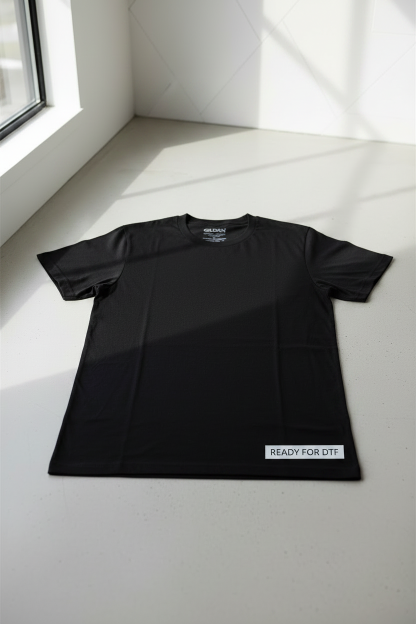 Black blank t-shirt laid flat on a light studio floor near a window, with a “Ready for DTF” label in the corner